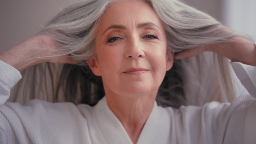 Gorgeous beautiful 60s old middle-aged mature Caucasian woman grandma senior older 50s lady smiling looking at camera at home pampering touching gray hair enjoy healthy hairstyle haircare procedure Royalty-Free Stock Footage #1095327241