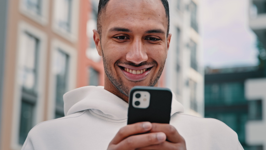 Joyful happy african latino man freelancer american guy stand on city street hold modern phone texting message make internet order search online media news distance communication use digital service Royalty-Free Stock Footage #1095327633