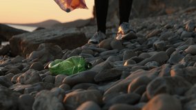 A volunteer walking down the pebble beach and collects plastic bottle. Coastal cleanup of trash for recycling. World environment day and Earth day. - Powered by Shutterstock - Get 15% off with code: PIKWIZARD15