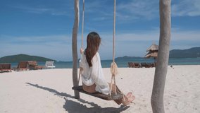 Young asian woman relaxing on swing beach sand in the beautiful sea island background, vacation concept