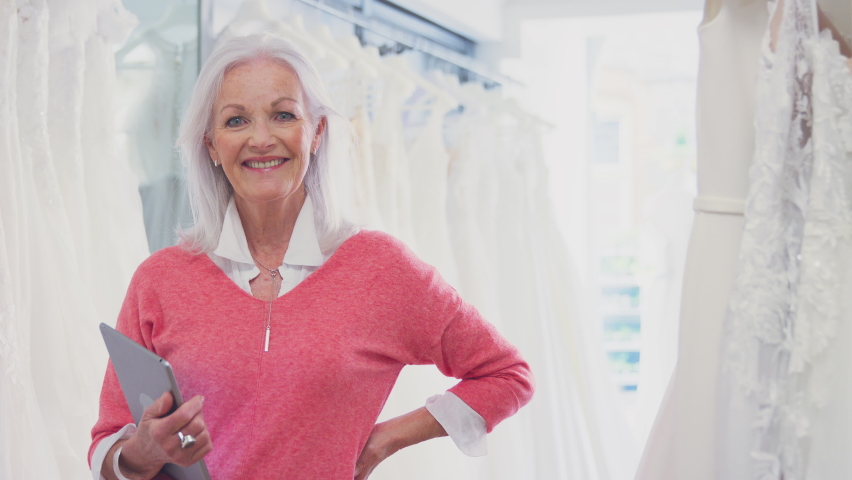 Portrait of female owner of bridal store looking through wedding dresses holding digital tablet - shot in slow motion