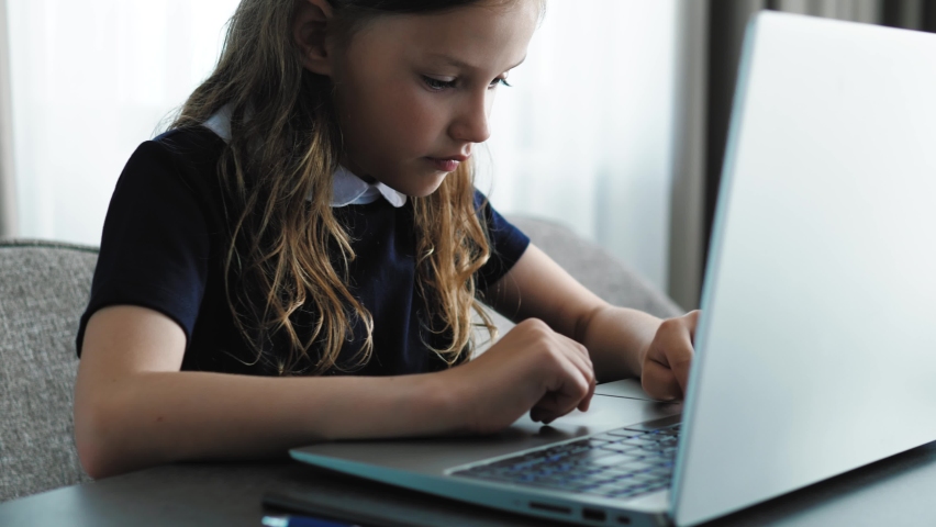 Concentrated focused female child teenager using pc laptop, chatting, scrolling, typing messages. Smart kid girl using laptop for online education, doing homework remotely