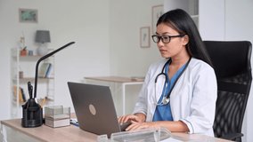 Asian female doctor therapist typing at laptop keyboard and browsing Internet while working in hospital office online. Telemedicine remote medical appointment, e-learning and online training concept