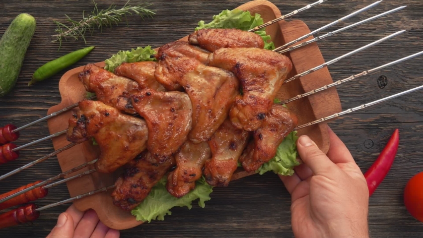 Top view of the hands placing a wooden plate full of delicious fried chicken wings on the skewers on the table