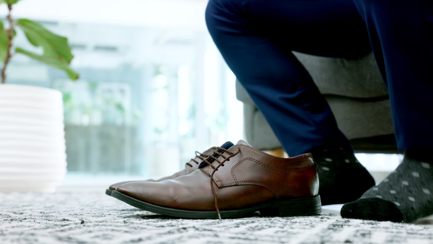 Shoes, fashion and hands with a business man getting ready and dressed for work in the living room of his home. Motivation, success and confident with a male employee tying his laces in the house