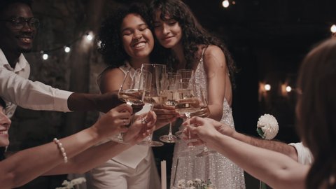 Lesbian newlyweds, their relatives and friends clinking glasses with champagne or sparkling wine at wedding party in evening 庫存影片