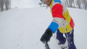 Slowmotion selfie video. A young man in a colorful jacket rides on a snowboard in a thick layer of snow