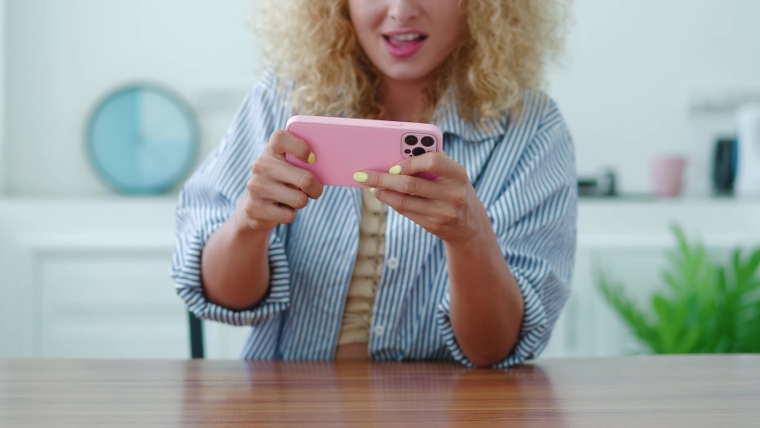 Selective focus on the hands of a red-haired excited youg blonde woman playing computer games, using her modern smartphone. Digital gadget addiction. Entertainment. Leisure.