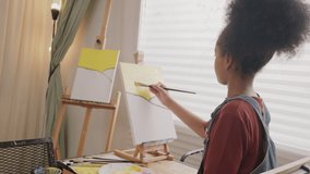 One young African American girl concentrates on acrylic color picture painting on canvas with a brush in art classroom, creative learning with talents and skills in elementary school studio education. - Powered by Shutterstock - Get 15% off with code: PIKWIZARD15