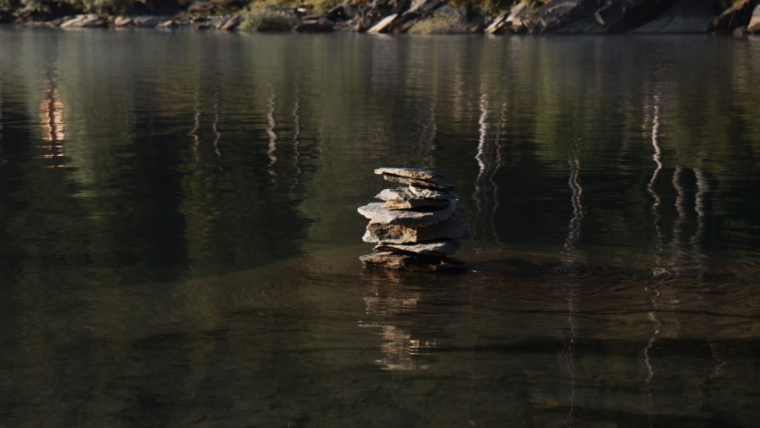 Stack of Stones Rocks on Water at Caumasee Lake Switzerland in Sunny Summer Morning, Stony Rocky Lakeside View with Reflections on Water Surface