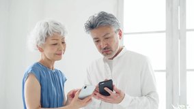Elderly Asian man and woman watching smart phones in the room.