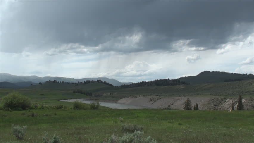 River in Yellowstone National Park surrounded by mountains, bushes and tall dry grass.