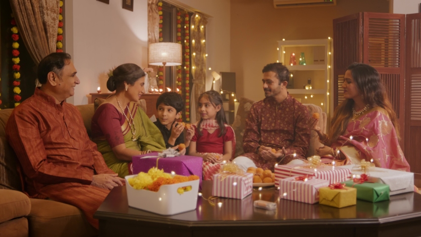 Happy smiling Hindu ethnic Indian family members in traditional Attire eating sweets (Laddoos, Laddus) enjoying the festivities together on the occasion of Diwali festival in a well decorated home. Royalty-Free Stock Footage #1095365085