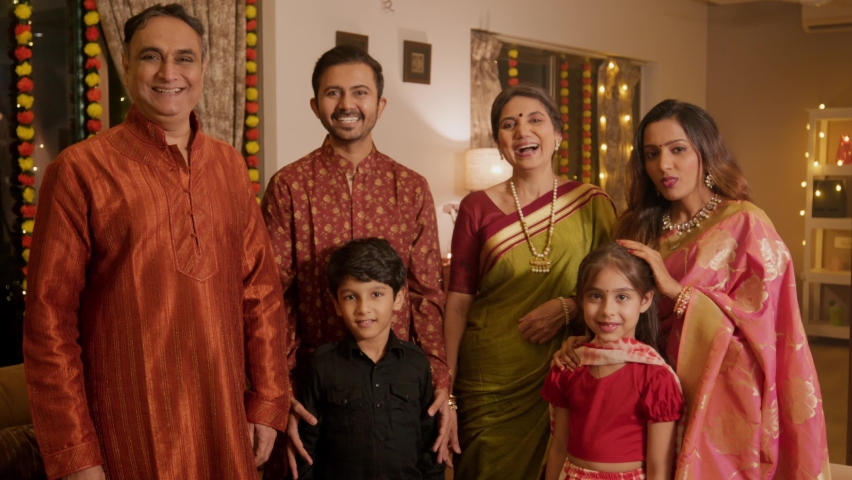 A happy smiling ethnic Indian Hindu family is standing together in traditional clothes including kids, parents, and grandparents looking at the camera during the Diwali festival in a decorated home Royalty-Free Stock Footage #1095365087