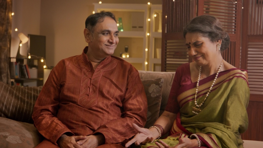 A happy Indian traditional Hindu elderly married couple where an old man or husband surprises his smiling ethnic wife in a saree with a jewellery gift box on the occasion of Diwali festival in a home. Royalty-Free Stock Footage #1095366443