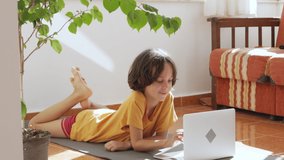 Distance learning. The boy lies on the floor at home and studies on a laptop. Children use technology