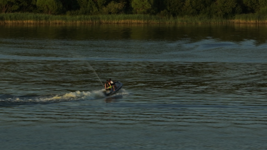 A jet ski rides on the water surface of the rivers in the evening. Two people have fun riding at aqua bike on a lake.