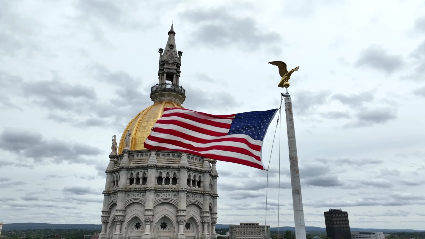 American flag waves by Hartford Connecticut state capitol dome. Aerial in Bushnell Park.