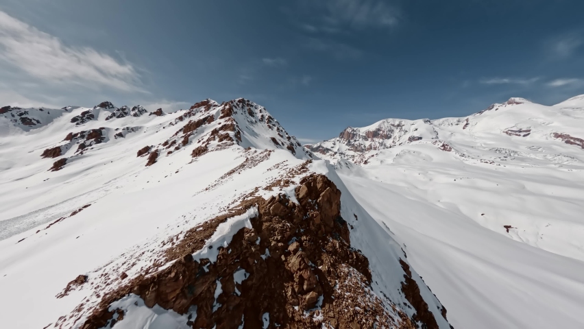 Aerial view flight climbing mountain summit cliff texture snow reversal dive from top ridge alpine sunny landscape. FPV sports drone epic rock scenery skyline panorama wild hilly valley freeze glacier Royalty-Free Stock Footage #1095377519