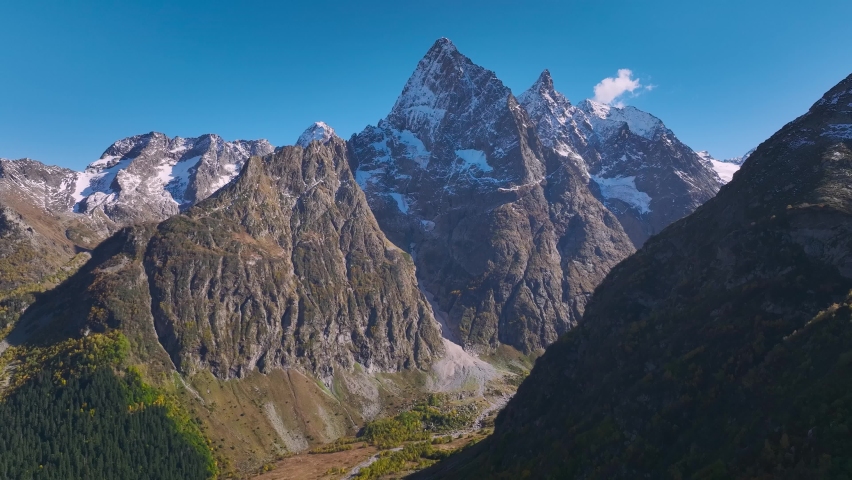Aerial view of a mountain valley with high mountains rocks and a river below. Alpine tourism in hard-to-reach natural locations. Sunny day. virgin nature
