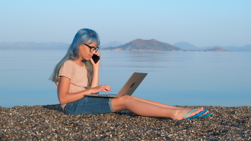 Teen uses a laptop on beach. A teen girl use a telephone and laptop during studing during summer vacation by the sea.