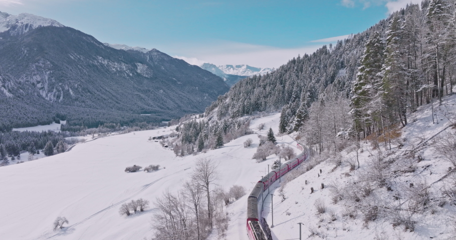 Aerial view of a world heritage sightseeing luxury Glacier and Bernina express in Swiss Alps snow winter scenery. Drone shot red train goes through the famous mountain in Filisur, Switzerland.