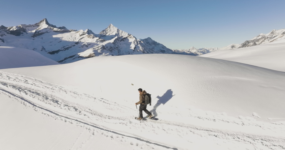 Aerial drone of Young man tourist hiker walking in snow shoes. Successful climber hiking up to mountain top swiss alps, Switzerland. Active travel lifestyle winter outdoor activities. Slow motion. Royalty-Free Stock Footage #1095386913