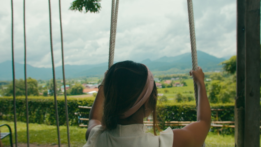 Happy girl from behind having fun on swing with scenery  mountain landscape view in slow motion