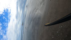 Person walking along sandy beach carrying surfboard, POV vertical video