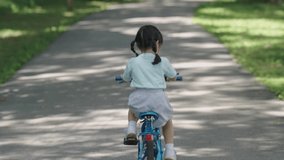 Video footage 4K of asian baby girl child learning to ride bicycle in the park garden. Education concept for kid practice cycling at park, baby sport concept.