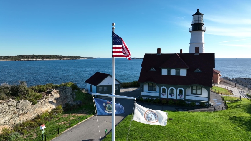 Portland Head Light. Cape Elizabeth and State of Maine flags fly with USA colors. Atlantic Ocean and Bay view.