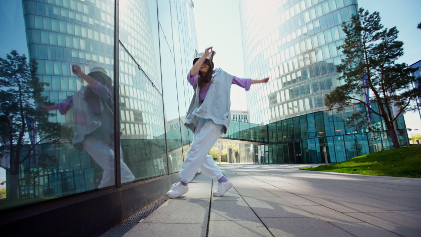 Fashionable funky caucasian girl dancer in sportswear is performing outdoor street dancing motion . slow motion video. Joyful summer female artist demonstrate choreography in the city. Royalty-Free Stock Footage #1095403743