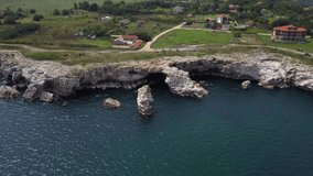 Aerial view of a rocky coastline and a small village with houses on a summer day. Roads with cars, hotels and harbor for boats are visible on the wooded plain. Bulgaria and the Black Sea