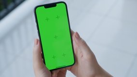Point of View of woman holds mobile phone iPhone and watching a video on the background of a floor with white tiles. Use green screen for copy space closeup. Chroma key mock-up on smartphone in hand. 