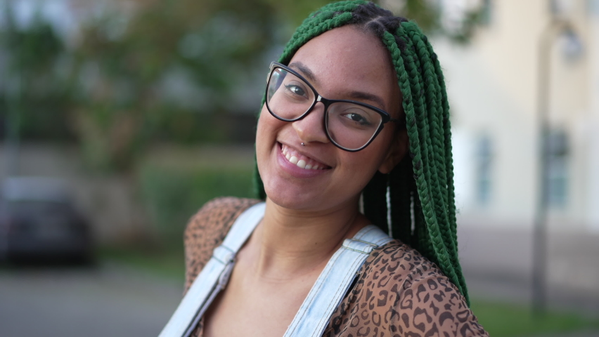 One happy young black woman with box braids hairstyle standing outside. South American laitna adult girl with braided fashion hair and glasses smiling
