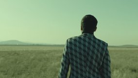 4K Rear , back view of man walking or standing on field . Young stylish lonely man on meadow field at day time . Shot on ARRI Alexa Camera in slow motion