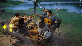 4K Group of Happy Asian man and woman enjoy and fun outdoor lifestyle travel nature camping in forest on summer holiday vacation. People friends playing guitar and having dinner together at night. - Powered by Shutterstock - Get 15% off with code: PIKWIZARD15