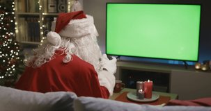 Happy Santa Claus sitting on the couch at home and playing video games, he is holding the gamepad and winning the match