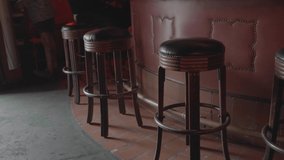 This panning video shows a line of wooden bar stools in dive bar.