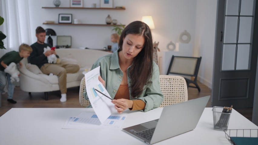 Young woman mother distance working online from home office while his family Husband and child daughter and son spending time at home. Busy mom using laptop computer sitting at table in homeoffice. Royalty-Free Stock Footage #1095413541