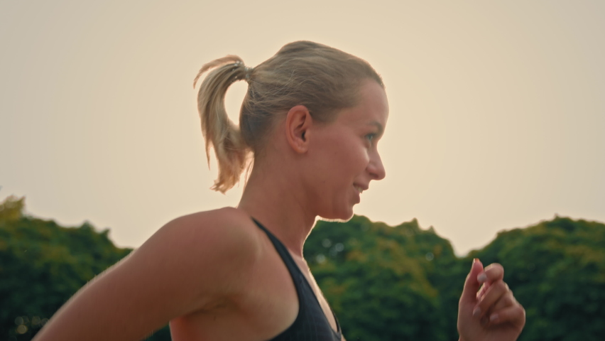 Side view athletic girl sportswoman runner jogger active fit woman running on city road training speed endurance jog in rays morning sun practice cardio sport exercise for race competition or marathon