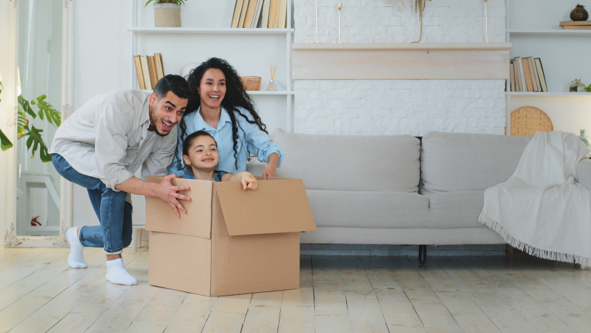 Multiracial multiethnic mother and father Indian Hispanic Caucasian parents push cardboard boxes with little cute child girl daughter ride inside homeowners family playing fun in new house relocation | Shutterstock HD Video #1095420155
