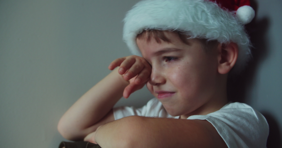 Portrait Cute boy in Christmas Hat Santa Clausa with big tears running down his cheeks, child sitting in corner lifestyle,tears are flowing with a screaming face. Child Sad