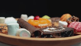 A sweets and colorful candy are rotating on the plate. Marshmallows and cake are unhealthy food. Concept of sugar and confection. Ungraded raw footage