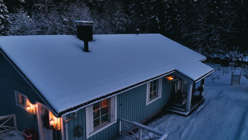 Drone analyzing the snow load on a house roof, during a gloomy, winter evening