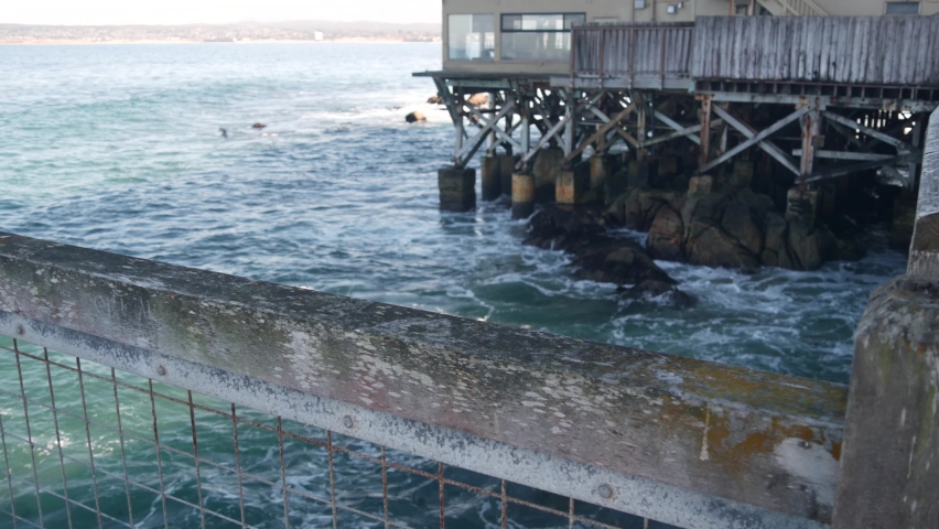 Waterfront wooden boardwalk in Monterey, California USA. Beachfront promenade on piles, pillars or pylons by ocean sea water and bay aquarium on Cannery Row street. Tourist vacations waterside resort.