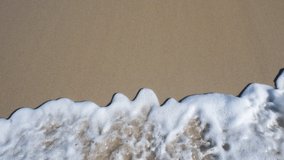 Top view slow motion Full HD video banner with sand, sea foam and waves. Scene of top view beach and seawater on sandy beach in summer. Nature and travel concept