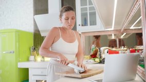 Female cutting fresh fish on cutting board preparing it for cooking and watching laptop . Healthy fresh sea food preparation and modern technology concept 4K video.