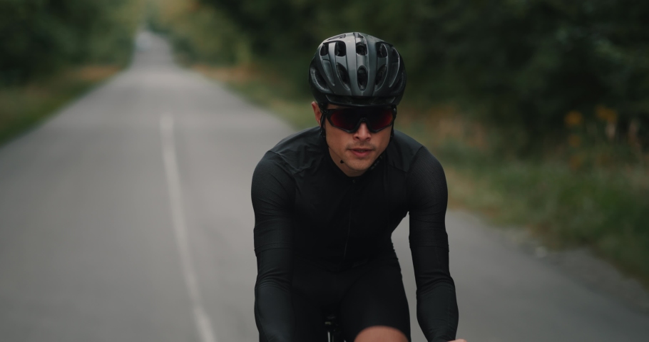 Man cyclist in helmet riding on a bicycle on road in the countryside. Professional triathlete in sportswear and glasses exercising in cycling on the highway | Shutterstock HD Video #1095457629