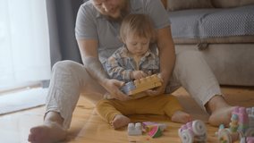 Happy young adult parent dad and child son play toys sit on floor carpet at home. Caring father having fun help cute kid build tower of wooden blocks. enjoy game activity give high five in living room